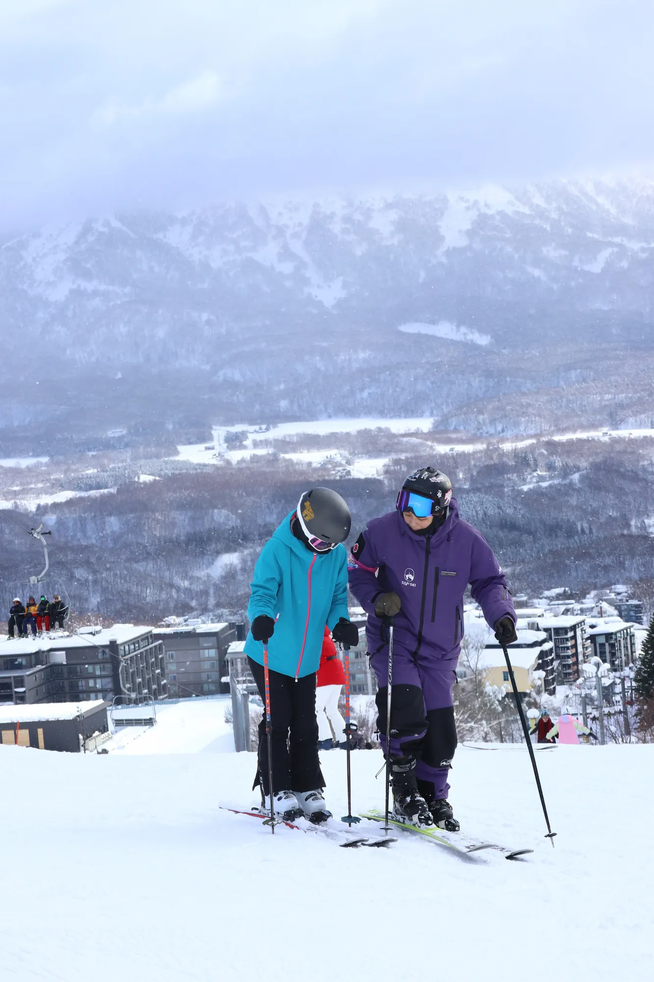 FUYU 教練在二世谷雪道上與學員一起,背景是比羅夫聚落
