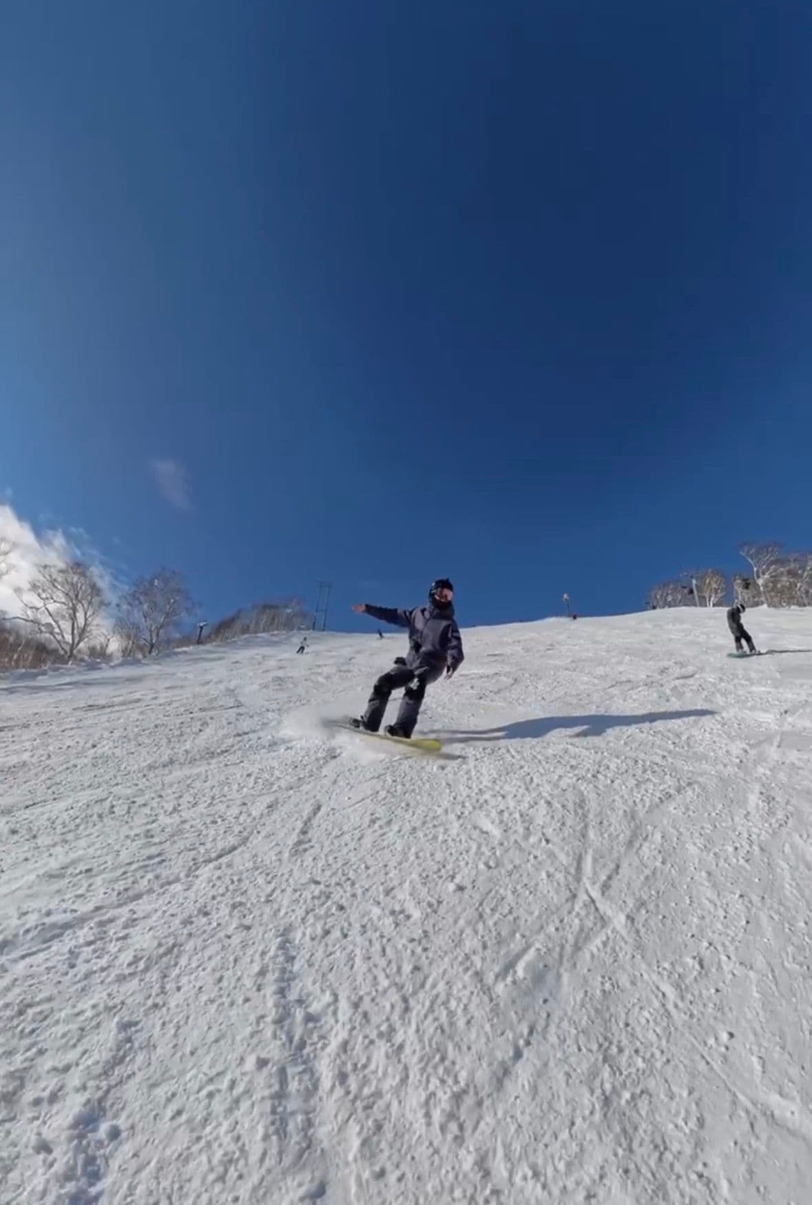 藍天下一位單板客在壓雪道上壓出一個轉彎,身後還有其他滑雪的人