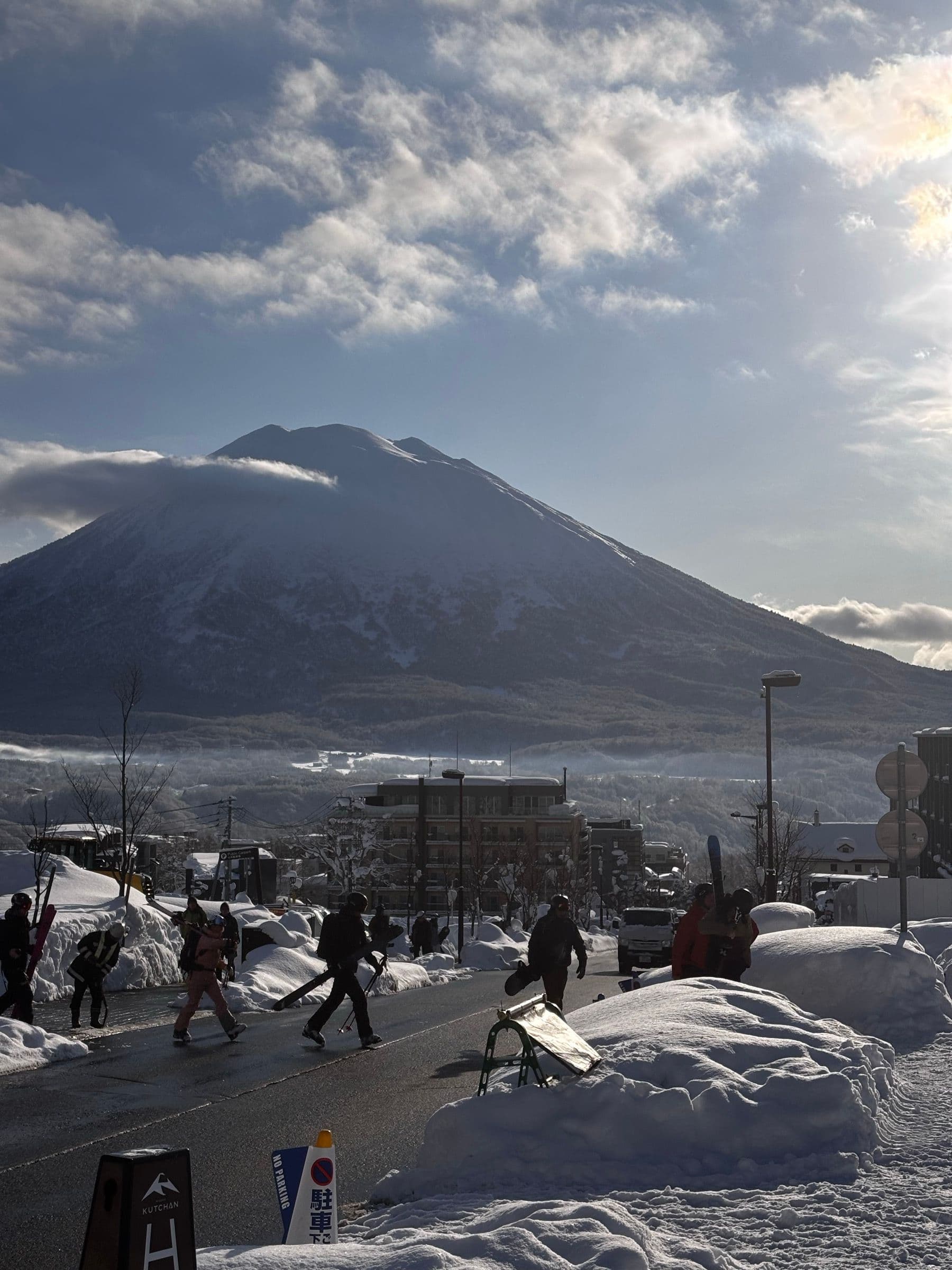 比羅夫街上滑雪客扛著雪具走過,兩旁是積雪的住宿建築,遠方是羊蹄山
