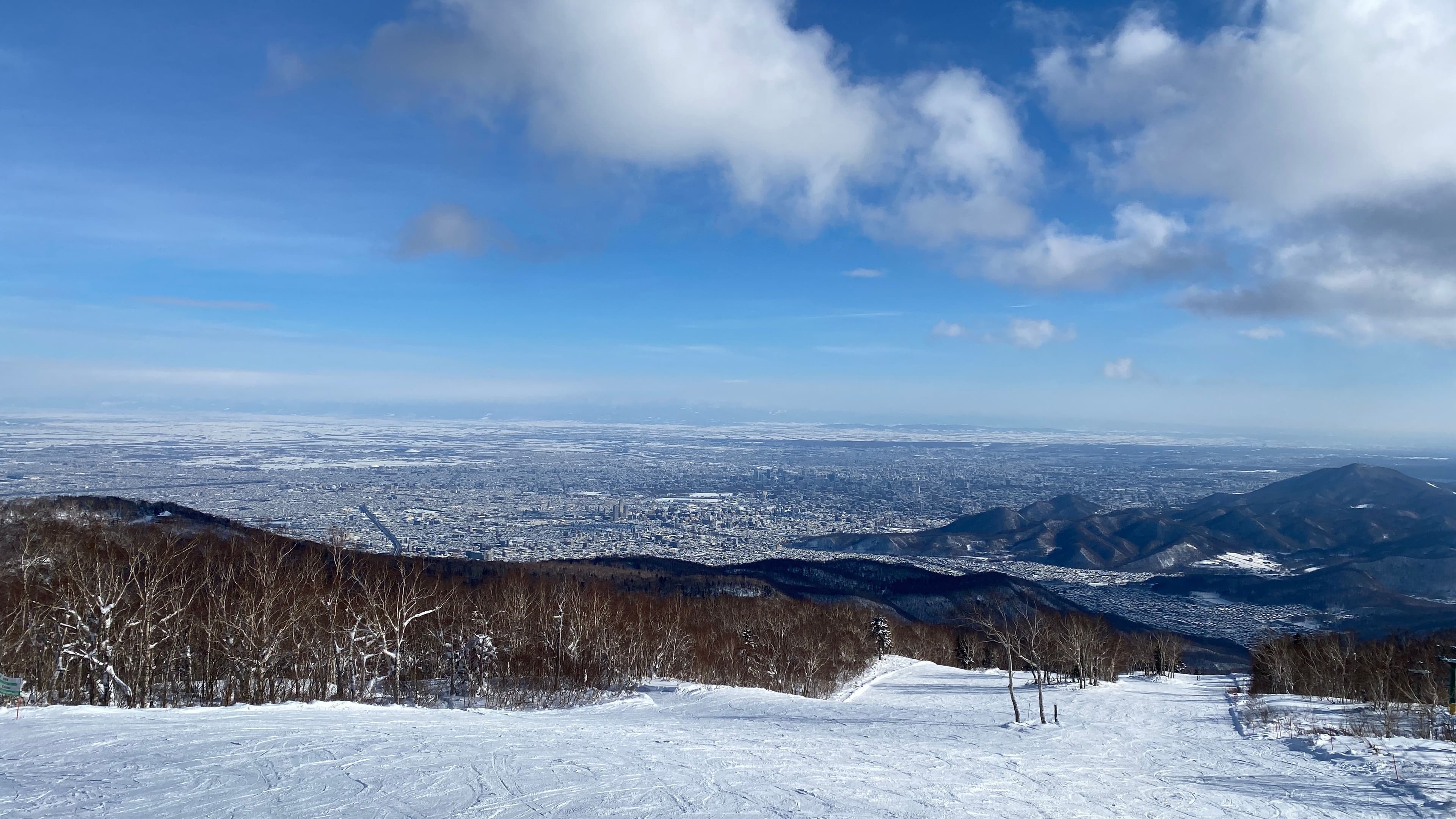 從手稻高地區山頂俯瞰,前景是雪道與白樺林,遠方是被雪覆蓋的札幌市區與石狩平原